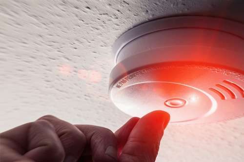 Security technician testing a commercial smoke detector to ensure operational excellence and safety.